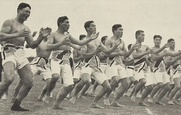 Recruits of the Maori Contingent performing a haka in a line on grass, a photograph from 1914